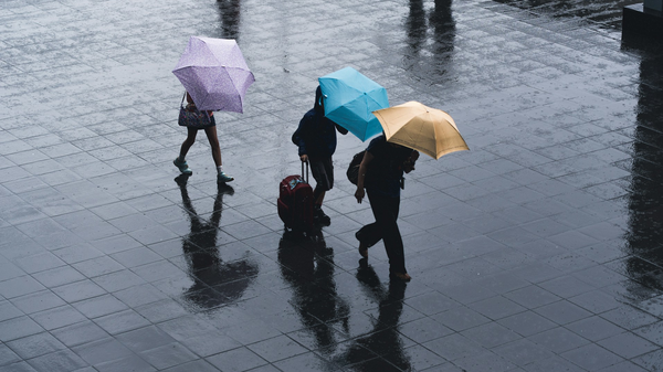 Drei Personen mit Regenschirm laufen über einen Platz