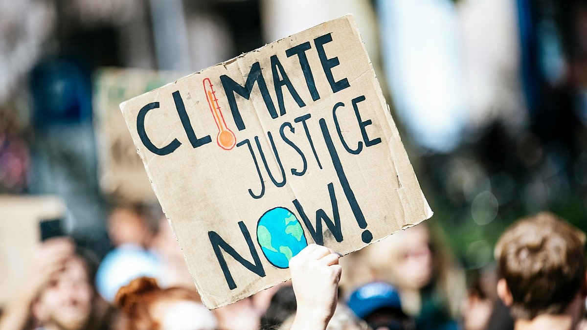 Ein Plakat mit der Aufschrift "Climate Justice Now" wird in die Höhe gehalten