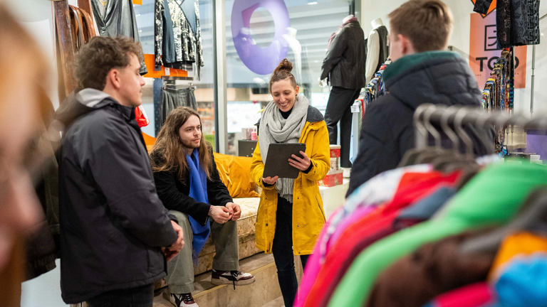 In einem Second Hand Modeladen in Stuttgart erläutert unser Guide Sabrina einer kleiner Gruppe die Vorteile von nachhaltiger Mode.